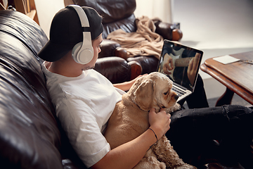 Image showing Young man sitting at home with his dog pet and listening to music during Coronavirus or Covid-19 quarantine. Lifestyle concept.