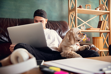 Image showing Young man working on laptop computer sitting at home with a dog pet and leaning during Coronavirus or Covid-19 quarantine