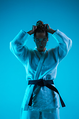 Image showing Portrait of professional female judoist isolated on blue studio background in neon light. Healthy lifestyle, sport concept.