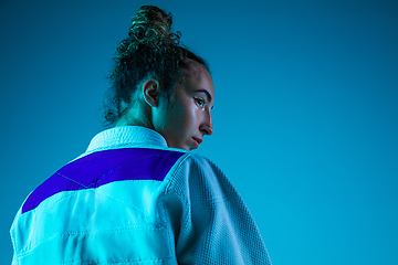 Image showing Portrait of professional female judoist isolated on blue studio background in neon light. Healthy lifestyle, sport concept.