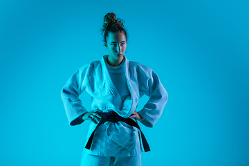 Image showing Portrait of professional female judoist isolated on blue studio background in neon light. Healthy lifestyle, sport concept.