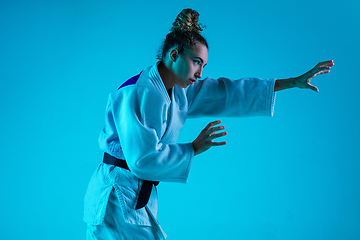 Image showing Professional female judoist training isolated on blue studio background in neon light. Healthy lifestyle, sport concept.