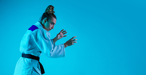 Image showing Professional female judoist training isolated on blue studio background in neon light. Healthy lifestyle, sport concept.