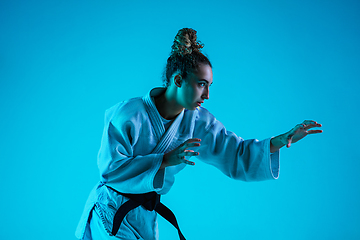 Image showing Professional female judoist training isolated on blue studio background in neon light. Healthy lifestyle, sport concept.