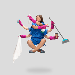 Image showing Female housemaid in pink gloves and blue uniform multitask like shiva isolated on gray background. Human emotions.