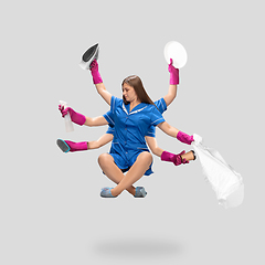 Image showing Young woman housemaid, cleaning worker in blue uniform multitask like shiva isolated on gray background.