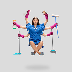 Image showing Female housemaid in pink gloves and blue uniform multitask like shiva isolated on gray background. Human emotions.