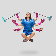 Image showing Young woman housemaid, cleaning worker in blue uniform multitask like shiva isolated on gray background.