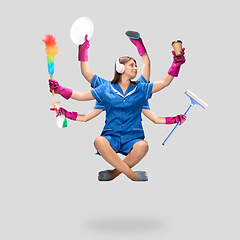 Image showing Young woman housemaid in headphones and blue uniform multitask like shiva isolated on gray background.