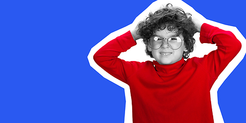 Image showing Portrait of young curly boy in red wear on blue studio background. Magazine style concept.