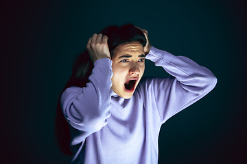 Image showing Close up portrait of young crazy scared and shocked woman isolated on dark background