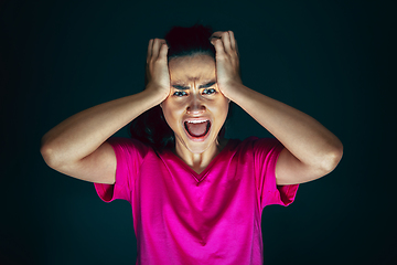 Image showing Close up portrait of young crazy scared and shocked woman isolated on dark background