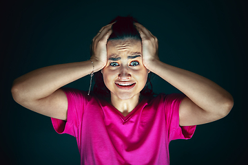 Image showing Close up portrait of young crazy scared and shocked woman isolated on dark background