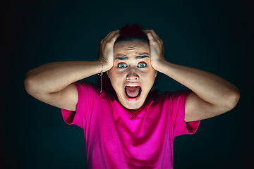 Image showing Close up portrait of young crazy scared and shocked woman isolated on dark background