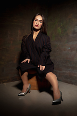Image showing Caucasian female inclusive model posing on dark studio background in classic black outfit