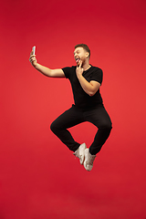 Image showing Full length portrait of young successfull high jumping man gesturing isolated on red studio background