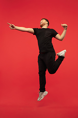 Image showing Full length portrait of young successfull high jumping man gesturing isolated on red studio background