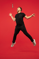 Image showing Full length portrait of young successfull high jumping man gesturing isolated on red studio background