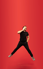 Image showing Full length portrait of young successfull high jumping man gesturing isolated on red studio background