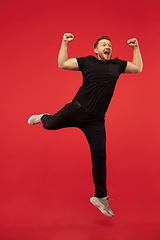 Image showing Full length portrait of young successfull high jumping man gesturing isolated on red studio background