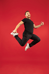 Image showing Full length portrait of young successfull high jumping man gesturing isolated on red studio background