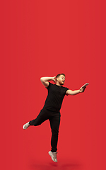 Image showing Full length portrait of young successfull high jumping man gesturing isolated on red studio background