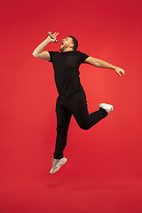 Image showing Full length portrait of young successfull high jumping man gesturing isolated on red studio background