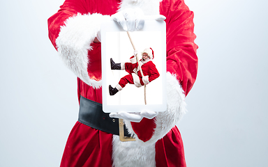 Image showing Close up hands of Santa Claus holding device with another climbing Santa on the screen