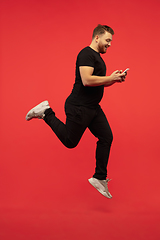 Image showing Full length portrait of young successfull high jumping man gesturing isolated on red studio background