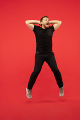 Image showing Full length portrait of young successfull high jumping man gesturing isolated on red studio background