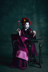 Image showing Young japanese woman as geisha on dark green background. Retro style, comparison of eras concept.