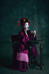 Image showing Young japanese woman as geisha on dark green background. Retro style, comparison of eras concept.