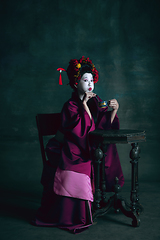 Image showing Young japanese woman as geisha on dark green background. Retro style, comparison of eras concept.