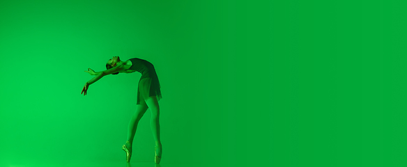 Image showing Young and graceful ballet dancer isolated on gradient green studio background in neon light. Art in motion