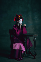 Image showing Young japanese woman as geisha on dark green background. Retro style, comparison of eras concept.