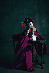 Image showing Young japanese woman as geisha on dark green background. Retro style, comparison of eras concept.