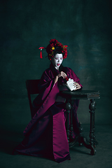 Image showing Young japanese woman as geisha on dark green background. Retro style, comparison of eras concept.