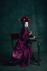 Image showing Young japanese woman as geisha on dark green background. Retro style, comparison of eras concept.