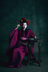 Image showing Young japanese woman as geisha on dark green background. Retro style, comparison of eras concept.