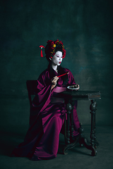 Image showing Young japanese woman as geisha on dark green background. Retro style, comparison of eras concept.