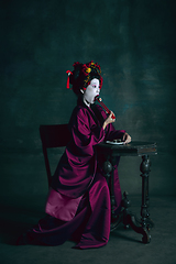 Image showing Young japanese woman as geisha on dark green background. Retro style, comparison of eras concept.