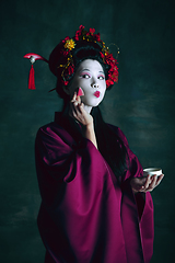 Image showing Young japanese woman as geisha on dark green background. Retro style, comparison of eras concept.