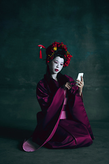 Image showing Young japanese woman as geisha on dark green background. Retro style, comparison of eras concept.