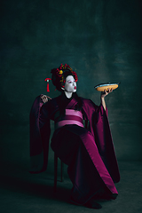 Image showing Young japanese woman as geisha on dark green background. Retro style, comparison of eras concept.