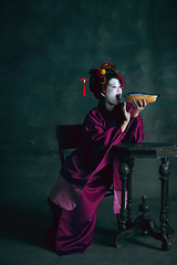 Image showing Young japanese woman as geisha on dark green background. Retro style, comparison of eras concept.