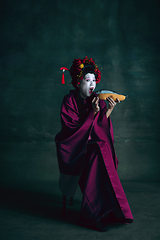 Image showing Young japanese woman as geisha on dark green background. Retro style, comparison of eras concept.