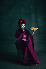 Image showing Young japanese woman as geisha on dark green background. Retro style, comparison of eras concept.