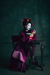 Image showing Young japanese woman as geisha on dark green background. Retro style, comparison of eras concept.