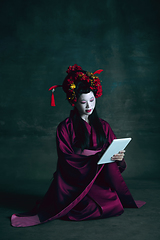 Image showing Young japanese woman as geisha on dark green background. Retro style, comparison of eras concept.