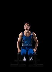 Image showing Muscular male gymnast training in gym, flexible and active. Caucasian fit guy, athlete in blue sportswear isolated on black